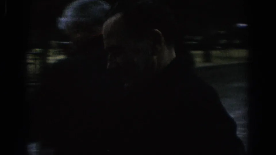 Dark 1966 Spain home-movie frame showing an adult man close to the camera with a second figure partly visible in the background.