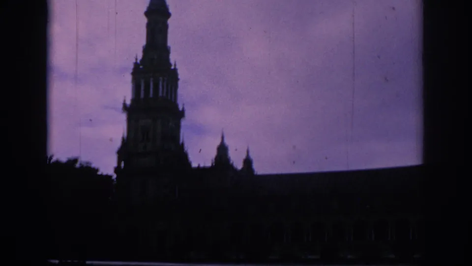 The visitor-shot view holds on a tall silhouetted tower and long facade, with the scene rendered dark by faded 8mm exposure.