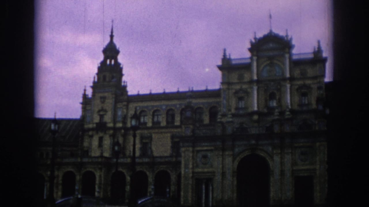 Closer view of ornate facade with tower, central entrance, arches, and cloudy sky.