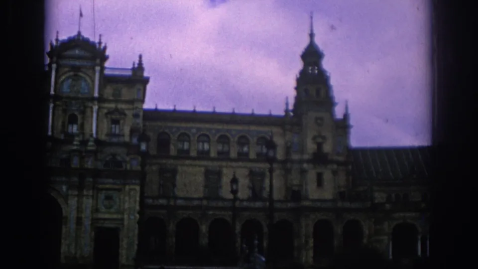 1966 Spain travel footage shows an angled view along Plaza de Espana, with tower, colonnade, decorative facade, and open courtyard.