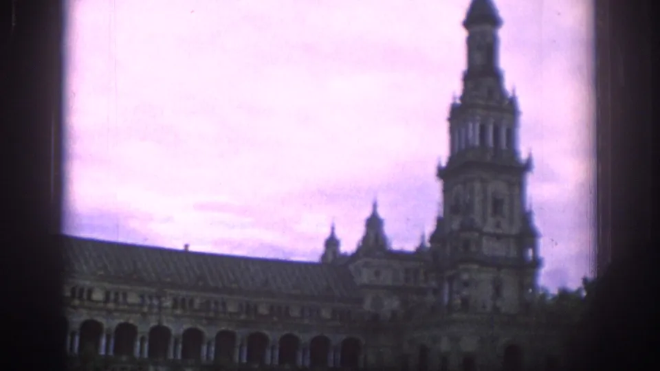 1966 Spain home-movie frame looking up at an ornate tower and arched building wing with purple color shift.