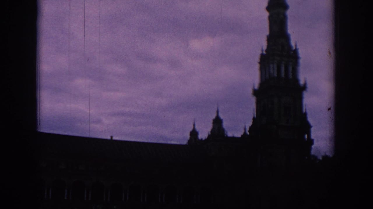 Dark silhouetted building with a tall spire and smaller roof ornaments under a purple sky.