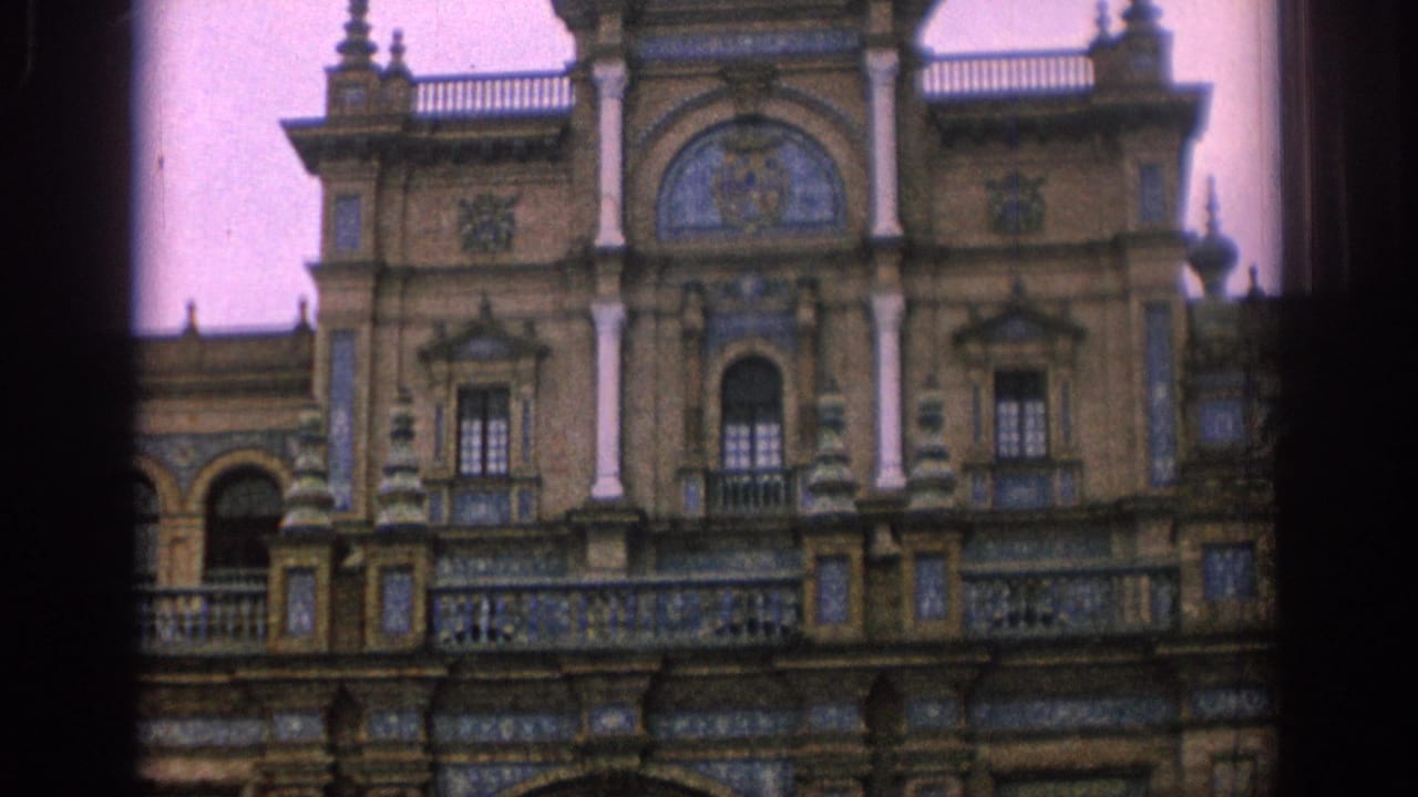 1966 Spain home-movie frame showing the upper facade of an ornate historic building with tile panels, columns, balconies, and arched openings.