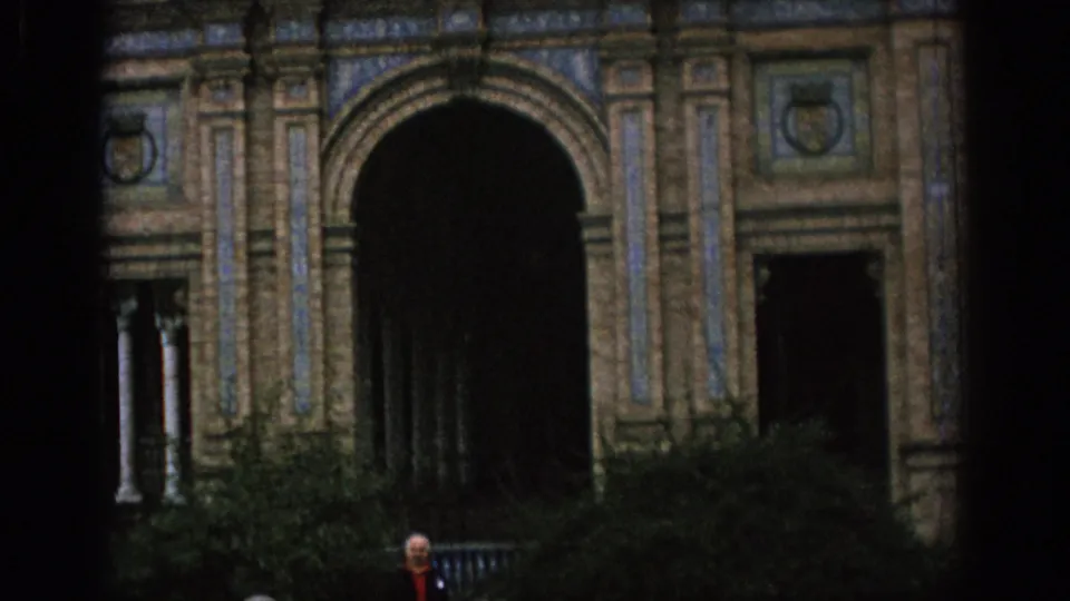 1966 Spain frame showing the base of the ornate facade, with a large dark archway, shrubs, and a person standing near the entrance for scale.