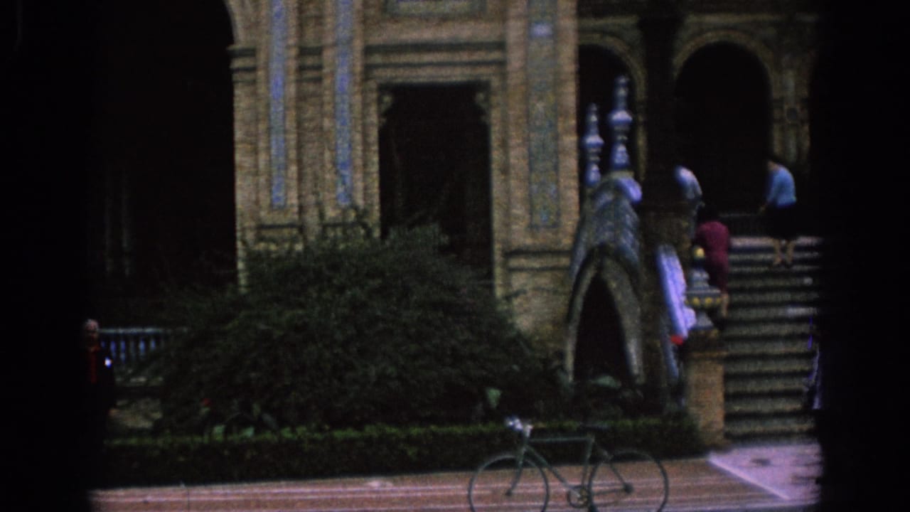 1966 Spain frame with broad stone stairs, ornate arches, shrubs, a parked bicycle, and visitors near the upper steps.