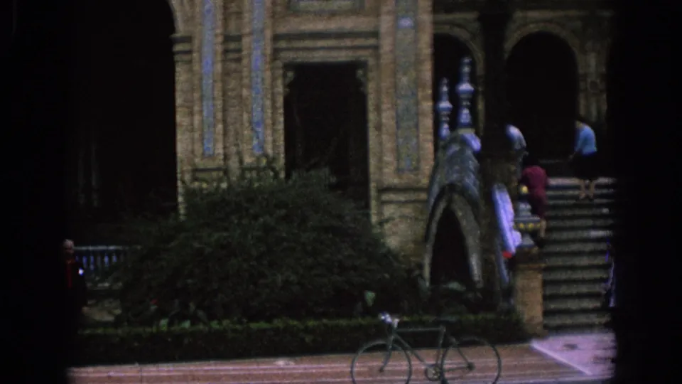 1966 Spain frame with broad stone stairs, ornate arches, shrubs, a parked bicycle, and visitors near the upper steps.
