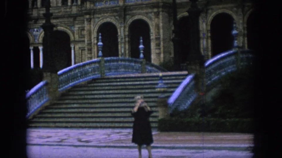 A 1966 Spain home-movie frame shows the tourist lifting her camera at Plaza de España in Seville.