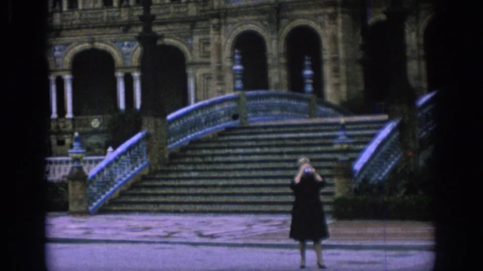 The visitor in a dark dress photographs the Plaza de España staircase in metadata-supported 1966 Spain footage.