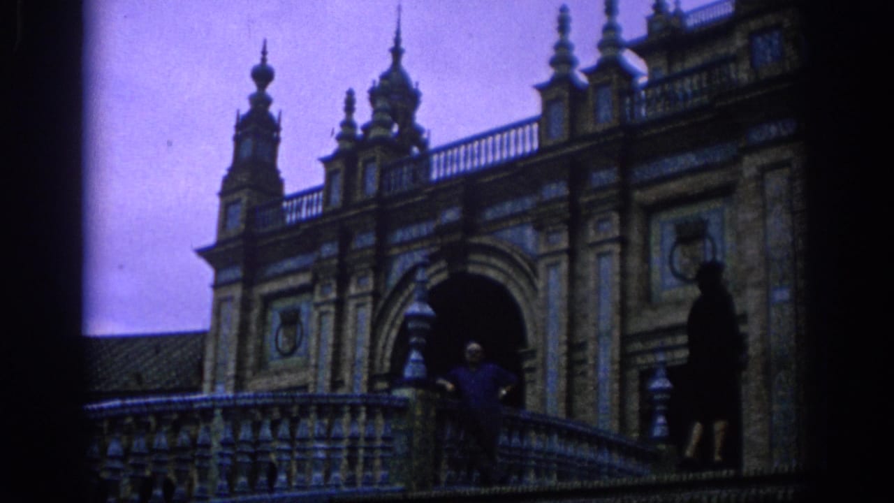 1966 Spain home-movie frame of a man and woman on a tiled balcony in front of arches and decorative spires.