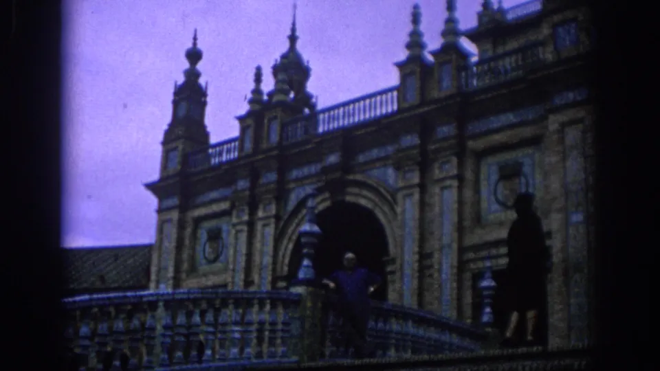 1966 Spain home-movie frame of a man and woman on a tiled balcony in front of arches and decorative spires.