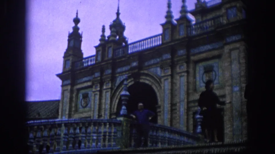 Wide 8mm view in Spain, 1966, showing two adults posing on a tiled balcony beneath arched architecture.