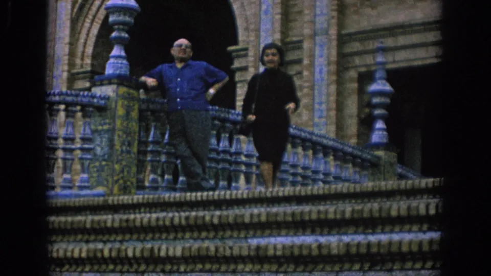 Closer 1966 Spain travel frame with a man in a blue short-sleeved shirt and a woman in dark dress on an ornate balcony.