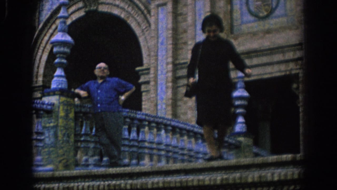 Man in a blue shirt leans by ornate tiled stairs as a woman walks down nearby.