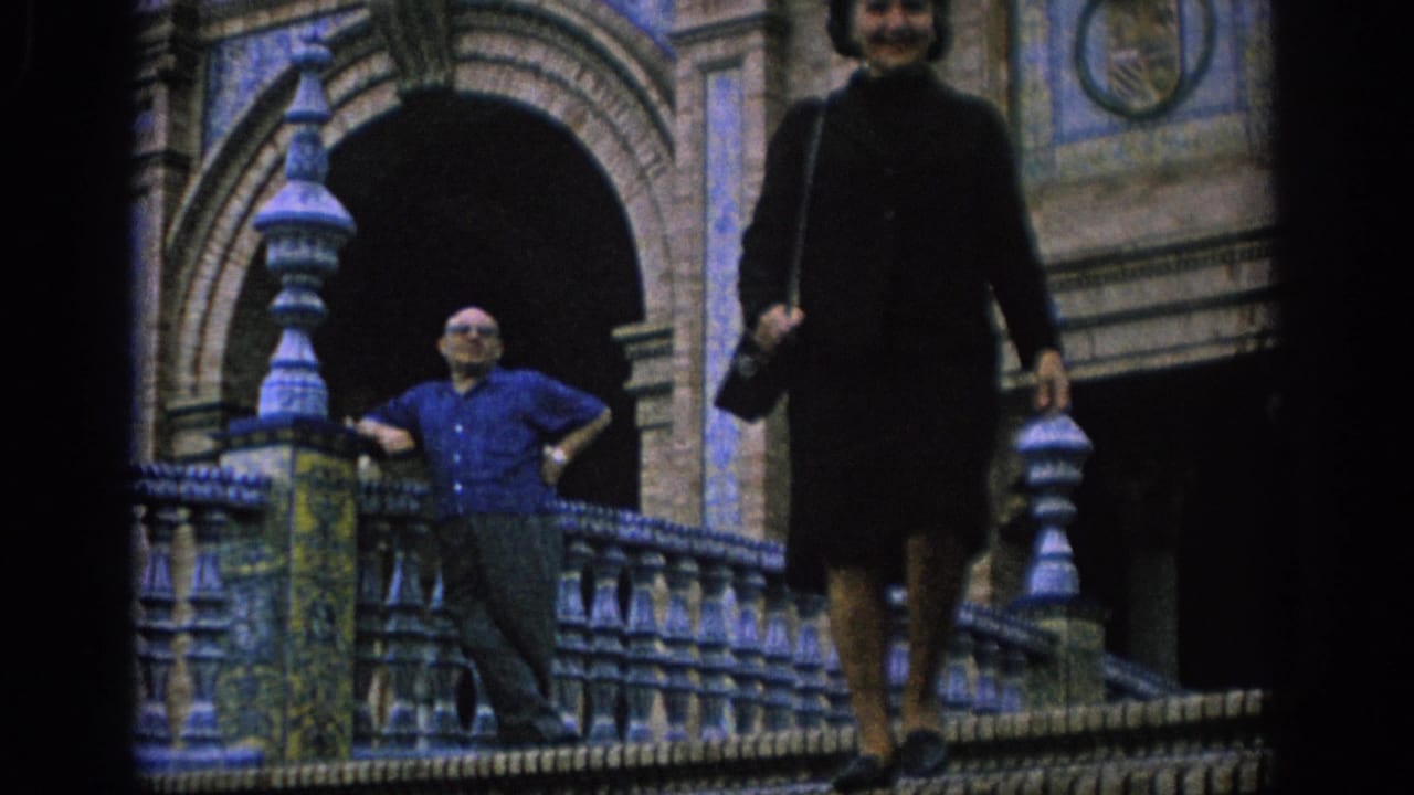 Woman in dark clothing walks down ornate tiled stairs past a man at the railing.