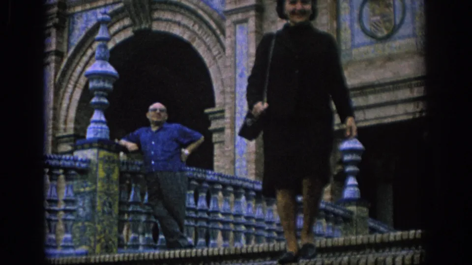 A woman descends an ornate tiled stairway at a Spanish landmark while a man in a blue shirt stands beside the balustrade.