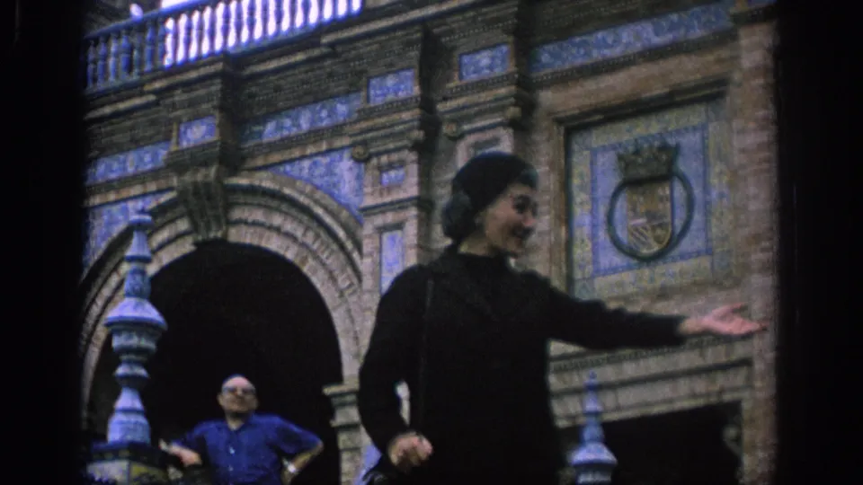 The woman extends her hand while descending the tiled stairs, with the man visible below against the historic facade.