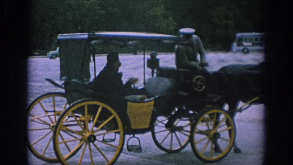 Side view of a horse-drawn carriage in Spain in 1966, showing passengers, yellow wheels, a coachman, trees, and a distant bus.