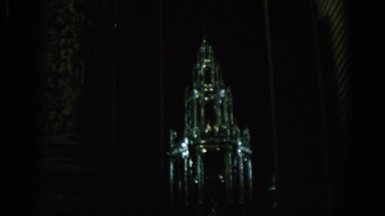 Dark interior with a small illuminated glass or crystal structure against shadowed columns.