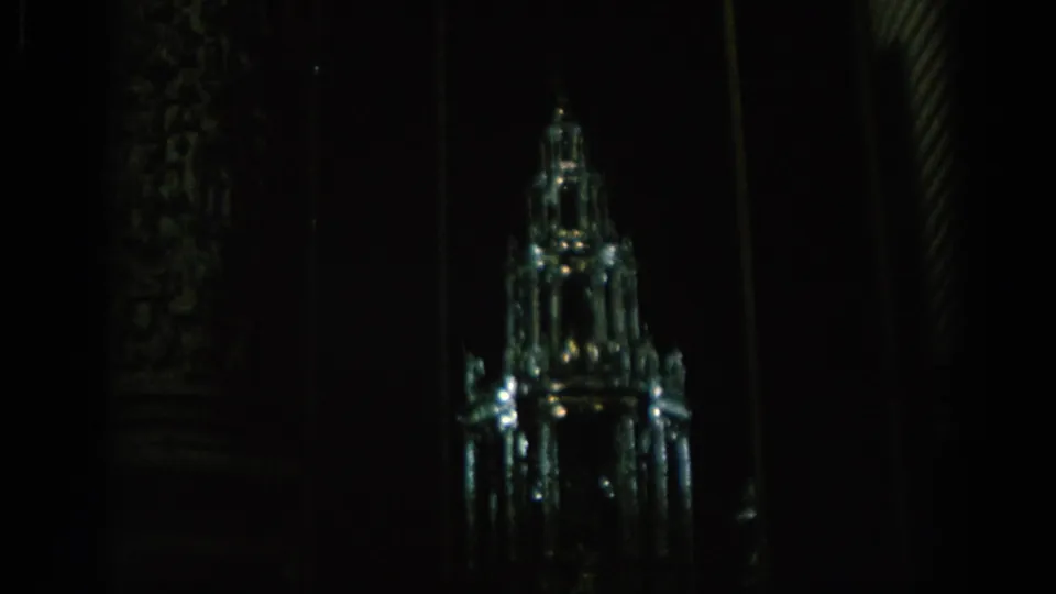 1966 Spain frame with a glowing glass or crystal miniature structure set against deep shadows and architectural columns.