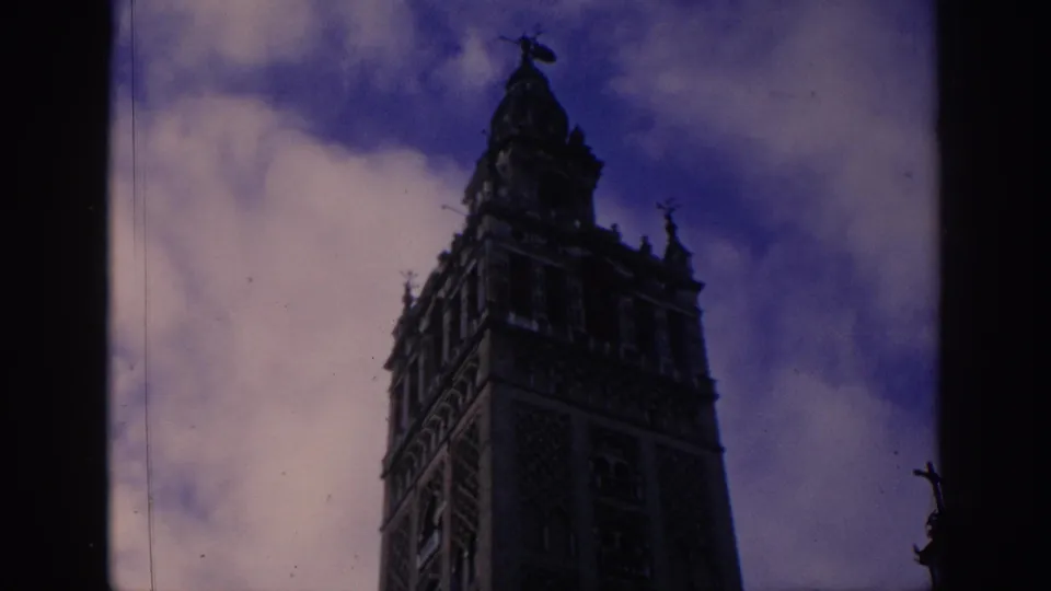 1966 Spain 8mm frame with the tower's upper architecture framed tightly beneath a blue-purple cloudy sky.