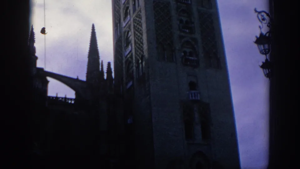 1966 Spain 8mm frame with Gothic cathedral stonework, narrow spires, a dark arch silhouette, and ornate street lamps.