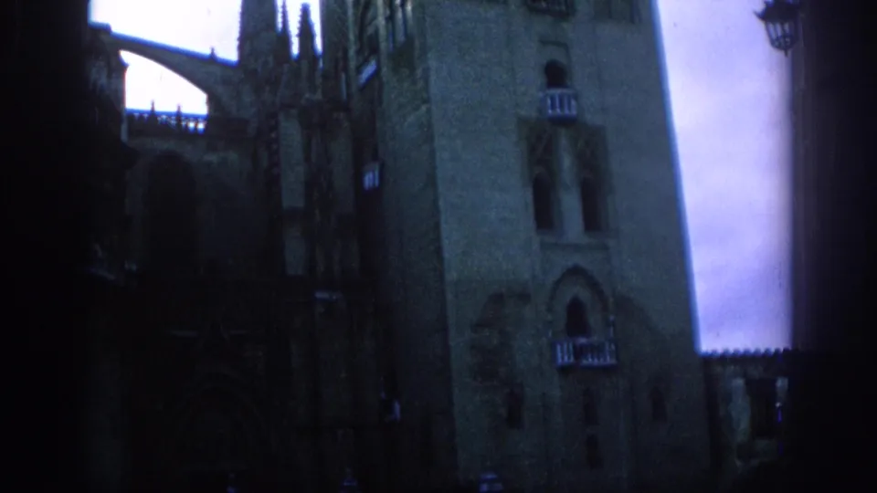 1966 Spain 8mm frame showing a low-angle Gothic cathedral exterior with tower stonework, spires, and deep shadow.