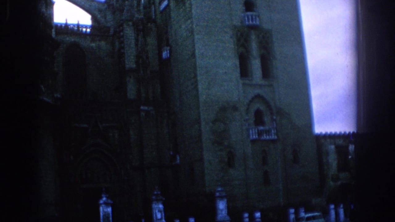 1966 Spain home-movie frame showing a shadowed stone castle or cathedral facade with tower forms, arched windows, and balcony-like details.