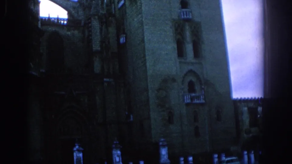 1966 Spain home-movie frame showing a shadowed stone castle or cathedral facade with tower forms, arched windows, and balcony-like details.