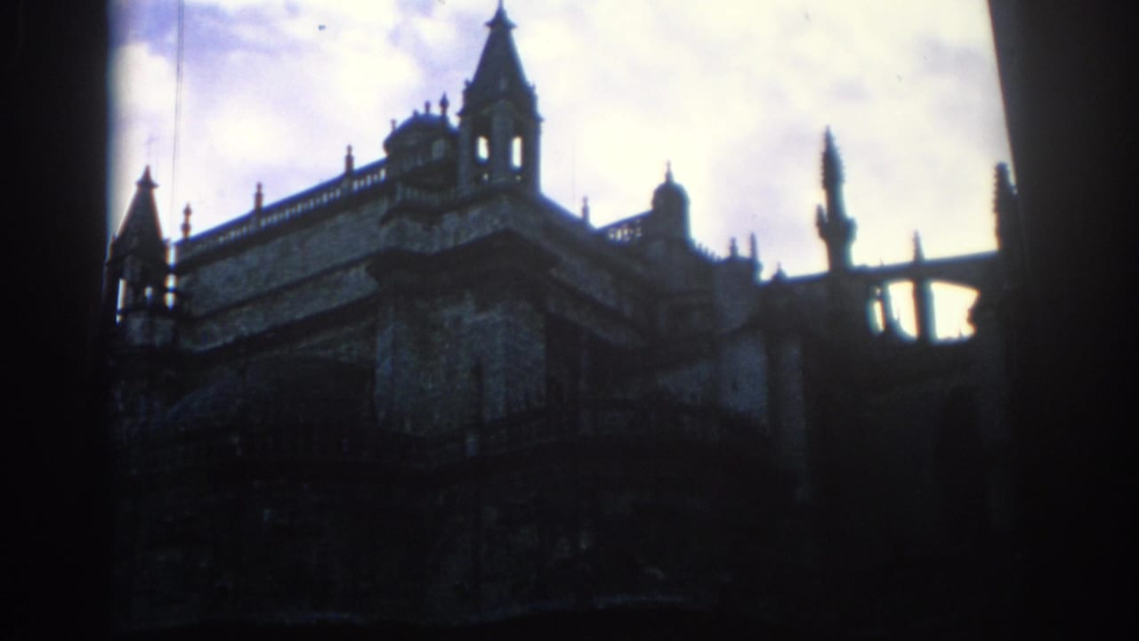 1966 Spain footage frame with the upper roofline of a castle-like or cathedral-like stone building silhouetted against a bright sky.