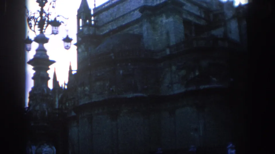 1966 Spain frame showing a decorative lamppost in front of a dark historic stone facade, with tower-like details and strong backlight.