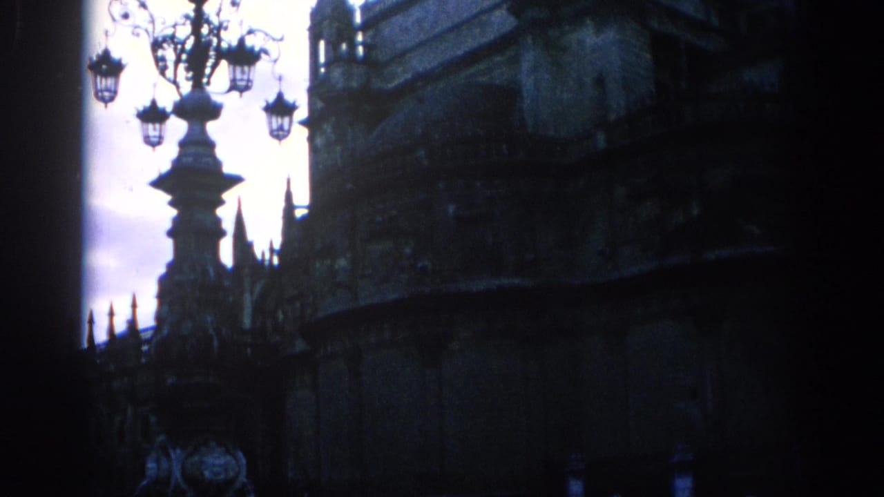 1966 Spain 8mm frame showing a shadowed Gothic stone facade and decorative street lamp silhouetted against a blue evening sky.