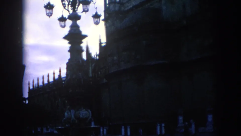 A visitor-shot 8mm view in Spain shows Gothic stonework, iron railings, and a decorative lamp in heavy dusk shadow.