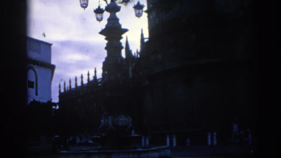 1966 Spain home-movie frame with a silhouetted lamp, railings, and Gothic architectural details seen from a low street angle.