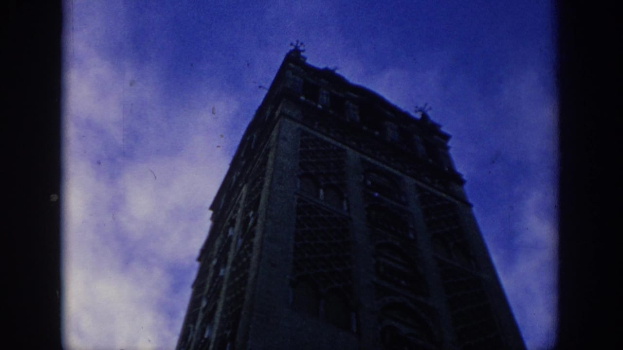 1966 Spain 8mm frame showing a Gothic cathedral tower rising dark against a blue twilight sky.