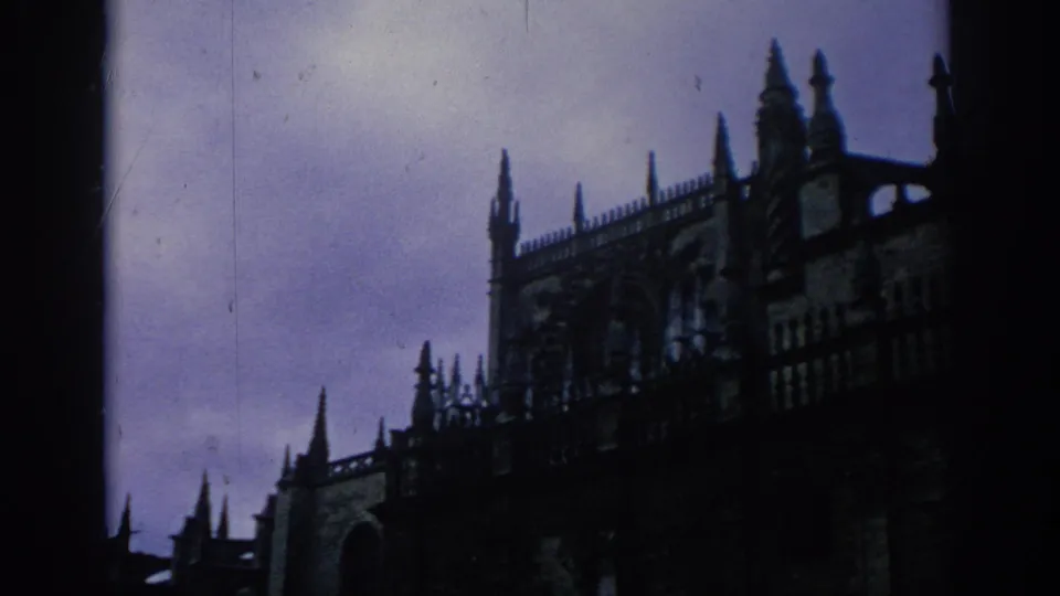 1966 Spain 8mm frame of a Gothic cathedral facade with spires and roof detail silhouetted at dusk.