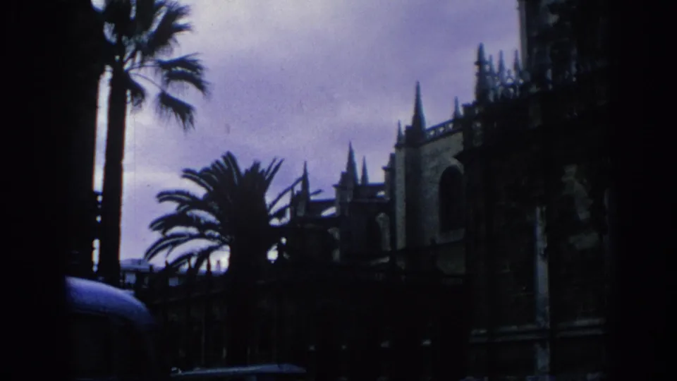 1966 Spain 8mm frame with palm trees in the foreground and a Gothic cathedral exterior in silhouette.
