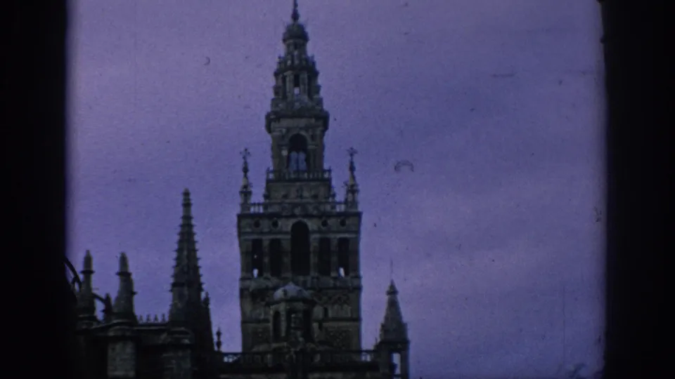 1966 Spain 8mm frame centering the Giralda tower with Seville Cathedral spires below a dim sky.