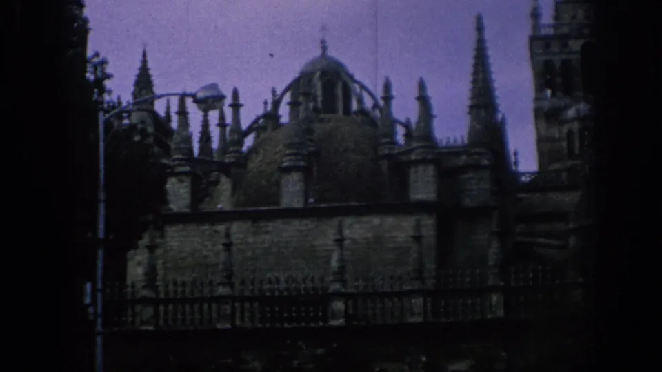 1966 Spain 8mm frame showing Seville Cathedral roof details, a dome, spires, railings, and part of the Giralda at dusk.