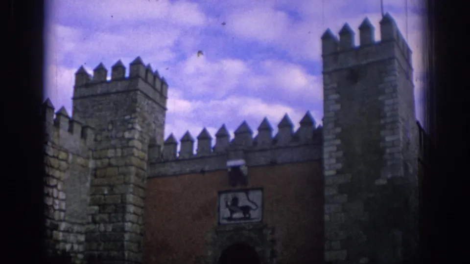 1966 Spain 8mm frame showing fortified stone towers, battlements, an arched entrance, and visible film-edge darkness.