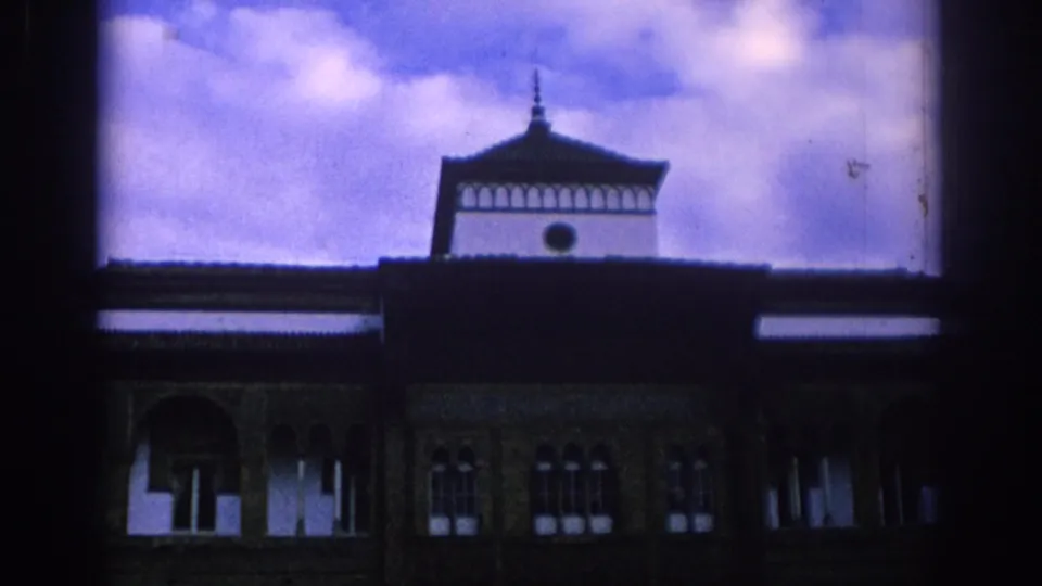 1966 Spain 8mm frame showing a traditional building facade with arched windows and a distinctive roofline beneath a cloudy sky.