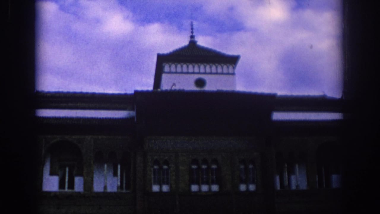 1966 Spain 8mm frame showing a Moorish-style facade with arched windows, dark roofline, and small tower against a purple-tinted sky.