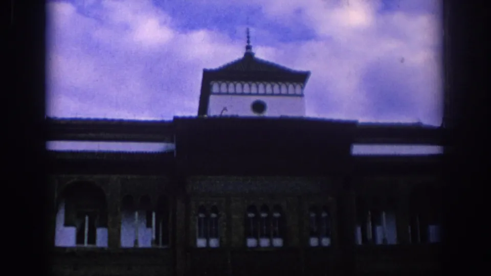 1966 Spain 8mm frame showing a Moorish-style facade with arched windows, dark roofline, and small tower against a purple-tinted sky.