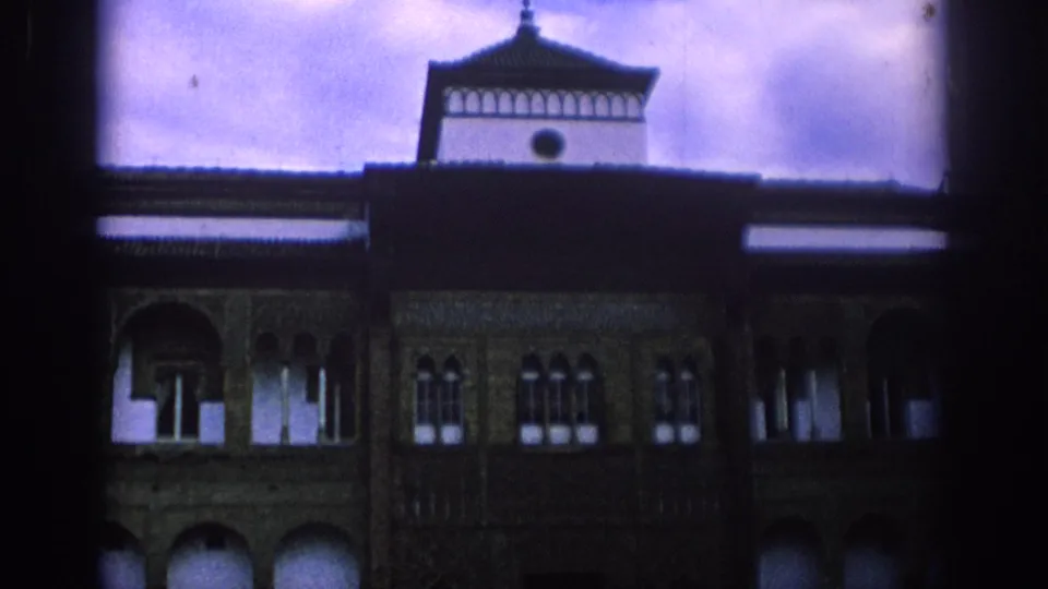1966 Spain home-movie frame with the building tower centered above a shadowed Moorish-style facade and rows of small arched windows.