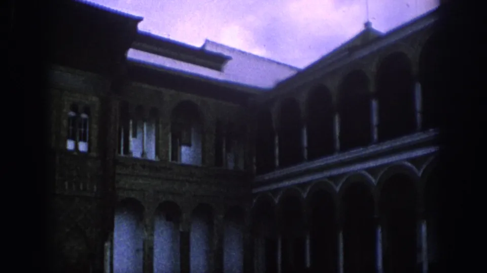 1966 Spain 8mm frame showing a shaded arcade, stone supports, decorative masonry and bright sky over the courtyard roof.
