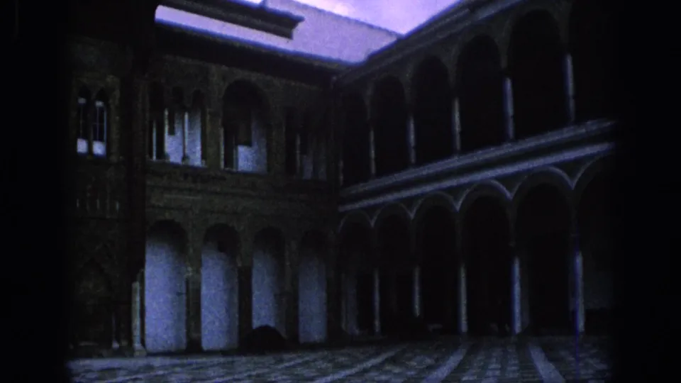 1966 Spain 8mm frame of a historic courtyard with arched colonnades, stone pillars, patterned paving and heavy interior shadows.
