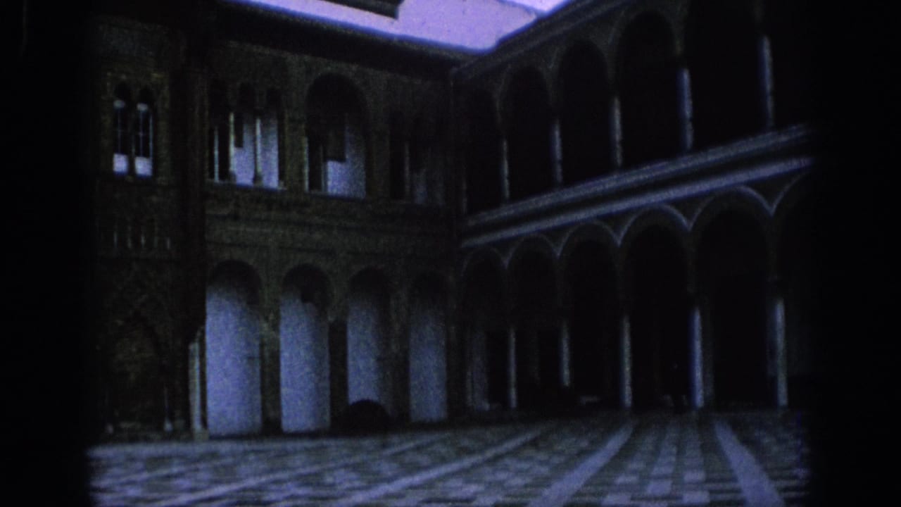 1966 Spain home-movie frame showing a dim historic cloister with arcades, columns, windows, and patterned paving.