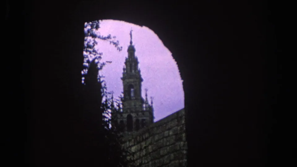 1966 Spain frame with a historic tower seen through a shadowed arch, with branches and a stone wall in silhouette.