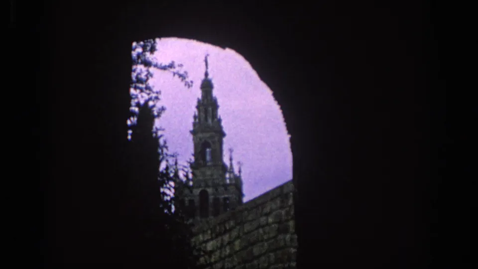 1966 Spain home-movie view of a tower glimpsed through an arched opening, with silhouetted foliage and masonry.