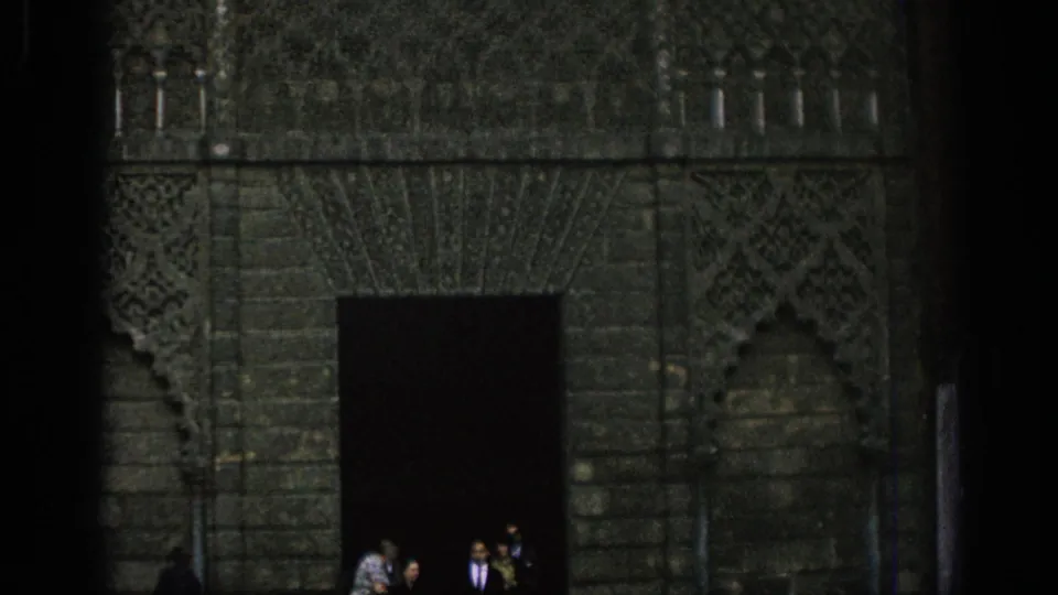 1966 Spain 8mm frame of visitors standing near a dark doorway in a heavily decorated historic stone facade.