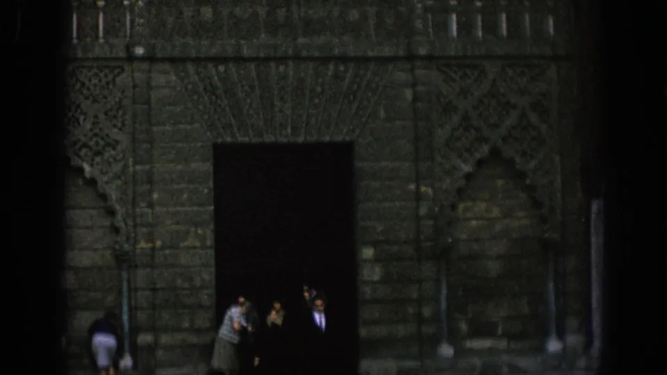 1966 Spain 8mm frame showing several visitors beside a shadowed doorway under ornate historic stonework.